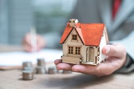 Ein Mann hält ein Miniaturhaus in der Hand